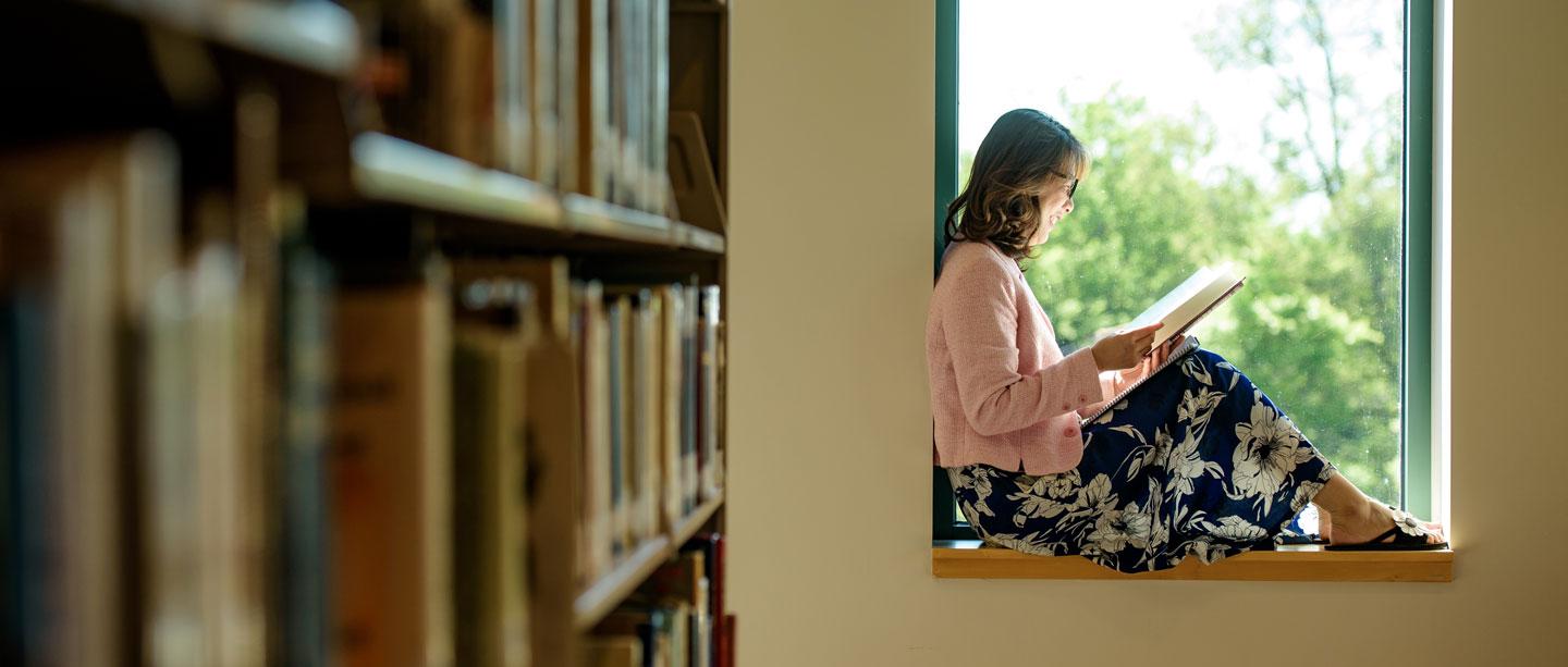 student reads a book next to window in library